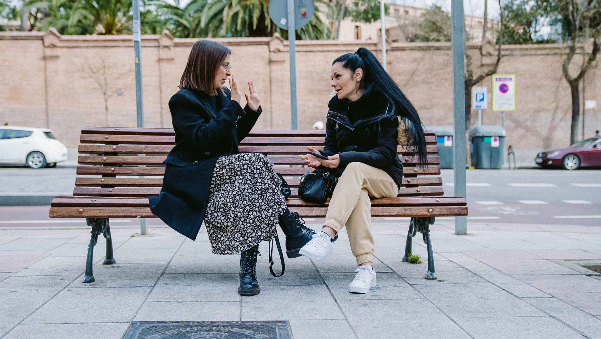 Maria and Helena are on a bench in the street having a friendly chat