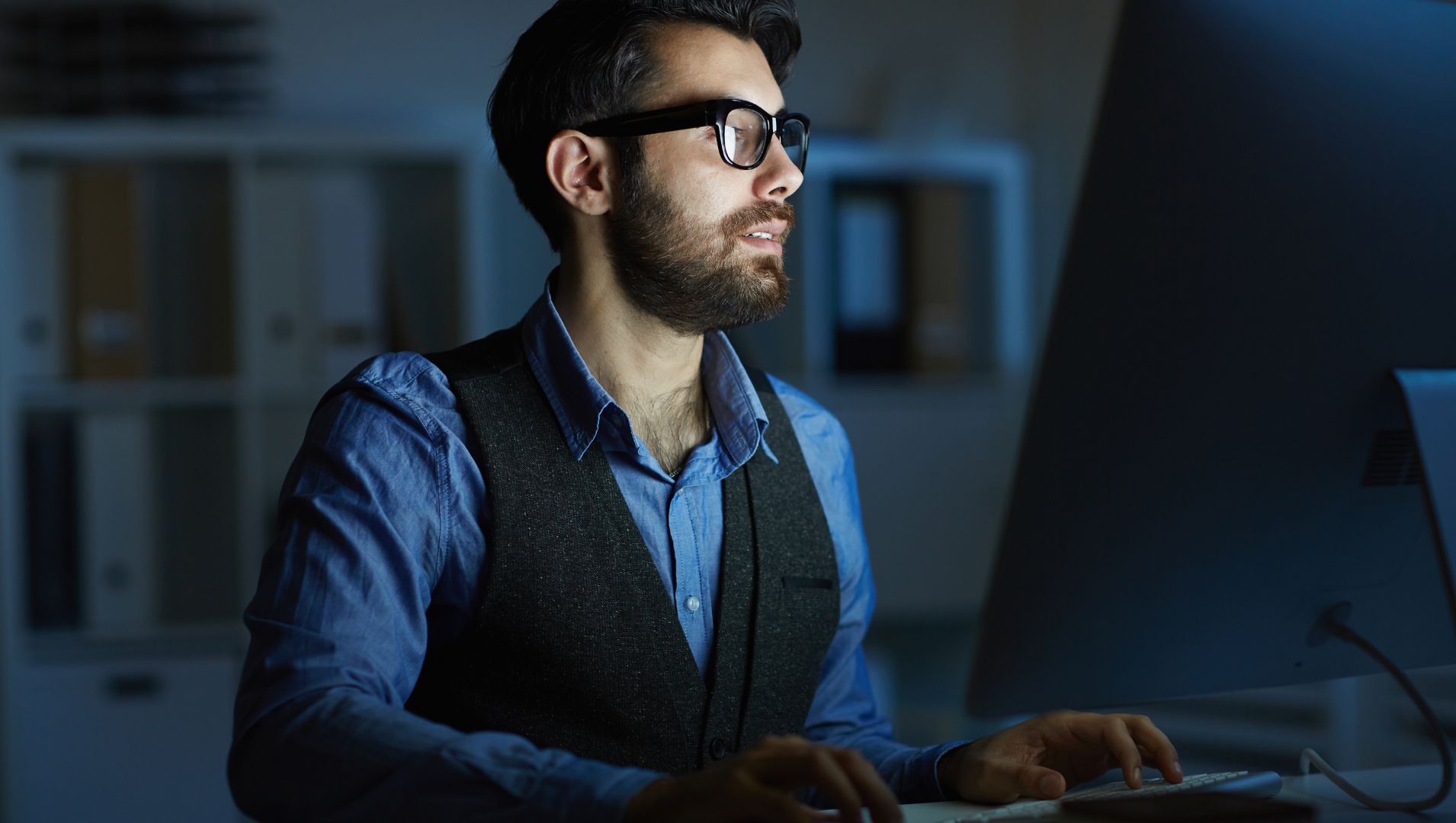 Man looks at a computer in a dark office at night