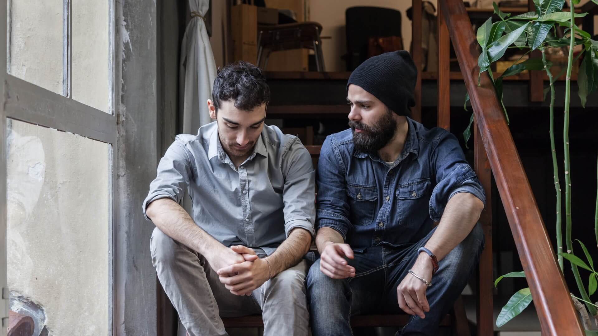 A man consoling his friend as they sit on some steps