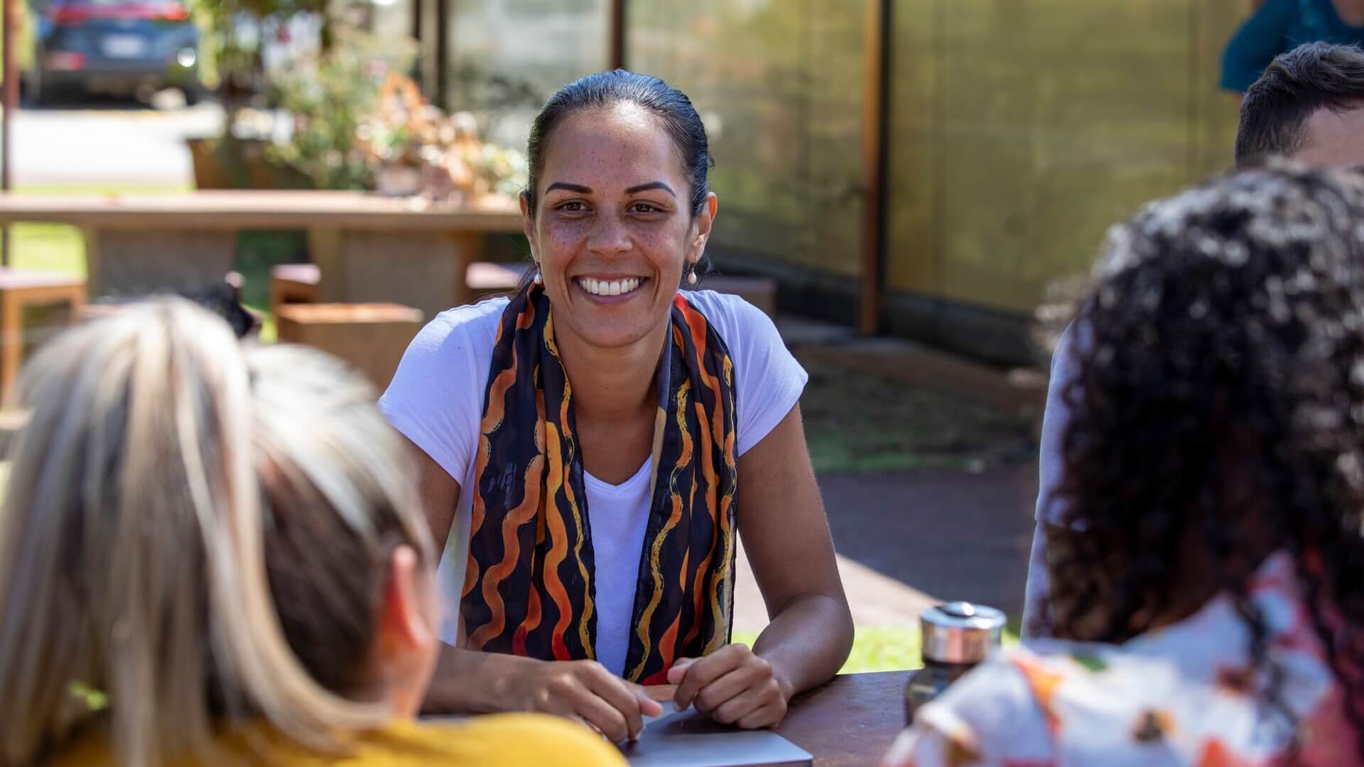 A woman sitting at a picnic table talking to two people