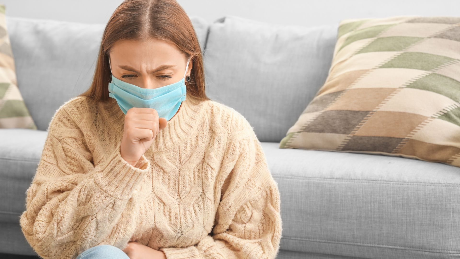 Person sitting on a couch with hand on stomach, indicating discomfort or digestive issues that may be linked to immunodeficiency.