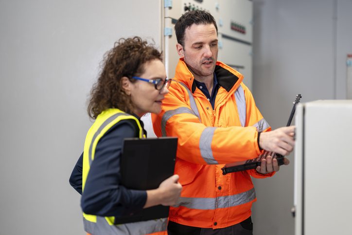 Two people in high-visibility vests looking at machinery