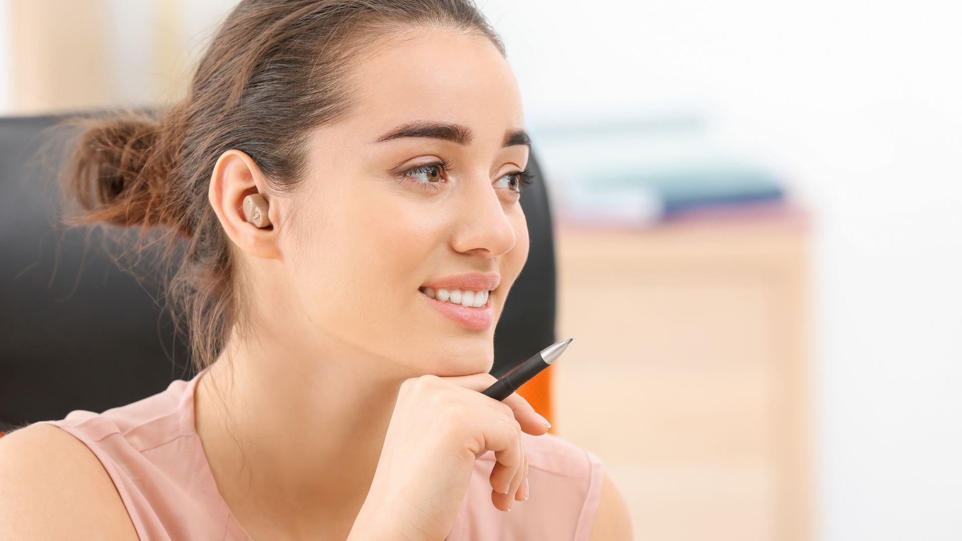 A woman smiles at her desk, she's wearing a small hearing aid.