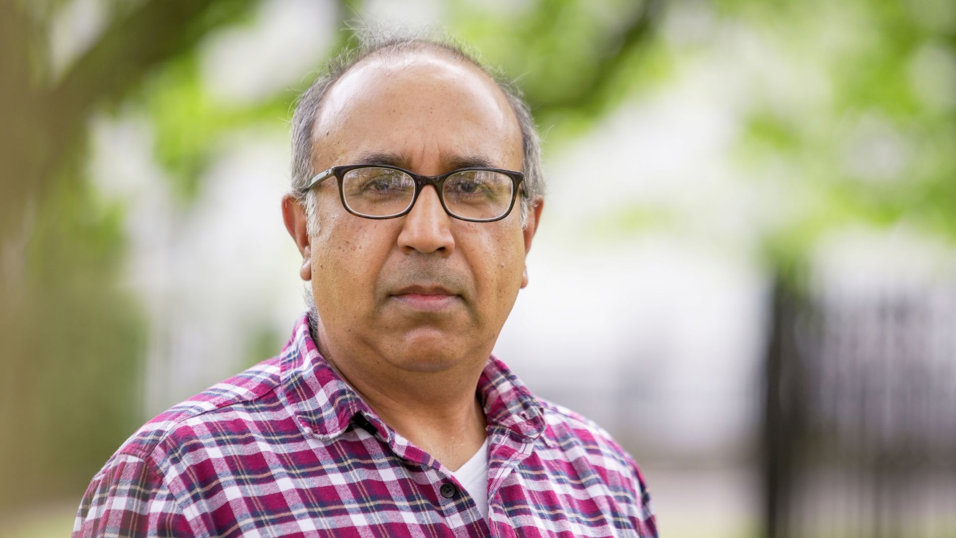 Portrait of Babu outdoors wearing a plaid shirt and glasses, symbolising confidence and new beginnings.