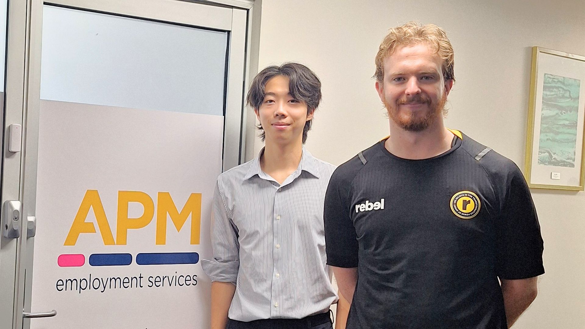 Workforce Australia participant Liam stands with an APM Employment Services consultant in the Surry Hills office. 