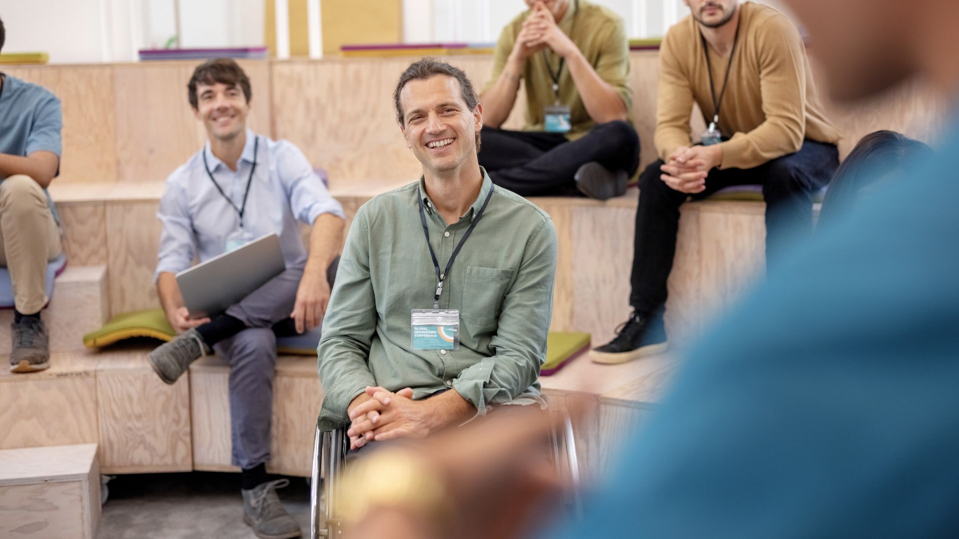 Group of people in a workplace training session listening to a speaker, including a man using a wheelchair, in an inclusive and supportive learning environment