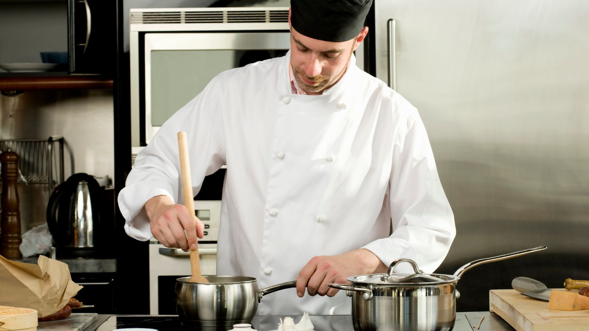 A chef prepares food in a saucepan in a kitchen