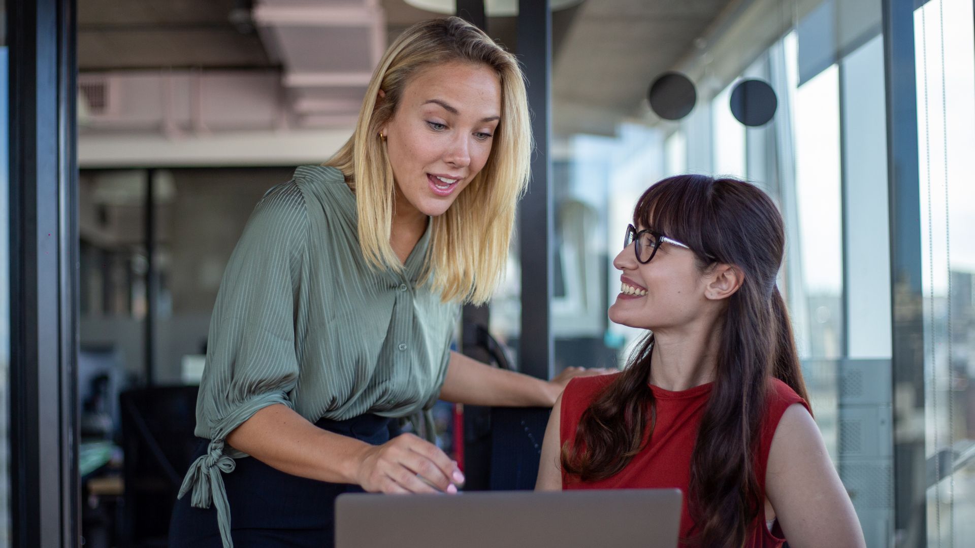 Two female colleagues talk infront of a desktop computer