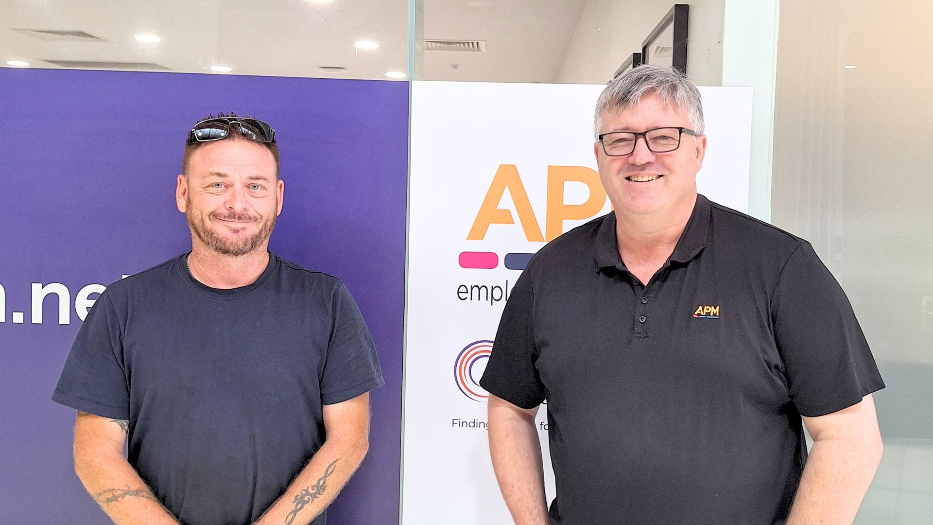 Self Employment Assistance participant Stephen stands with an APM consultant in an office setting. The image supports a story about building confidence, learning business basics, and starting a new business with support after feeling overwhelmed.