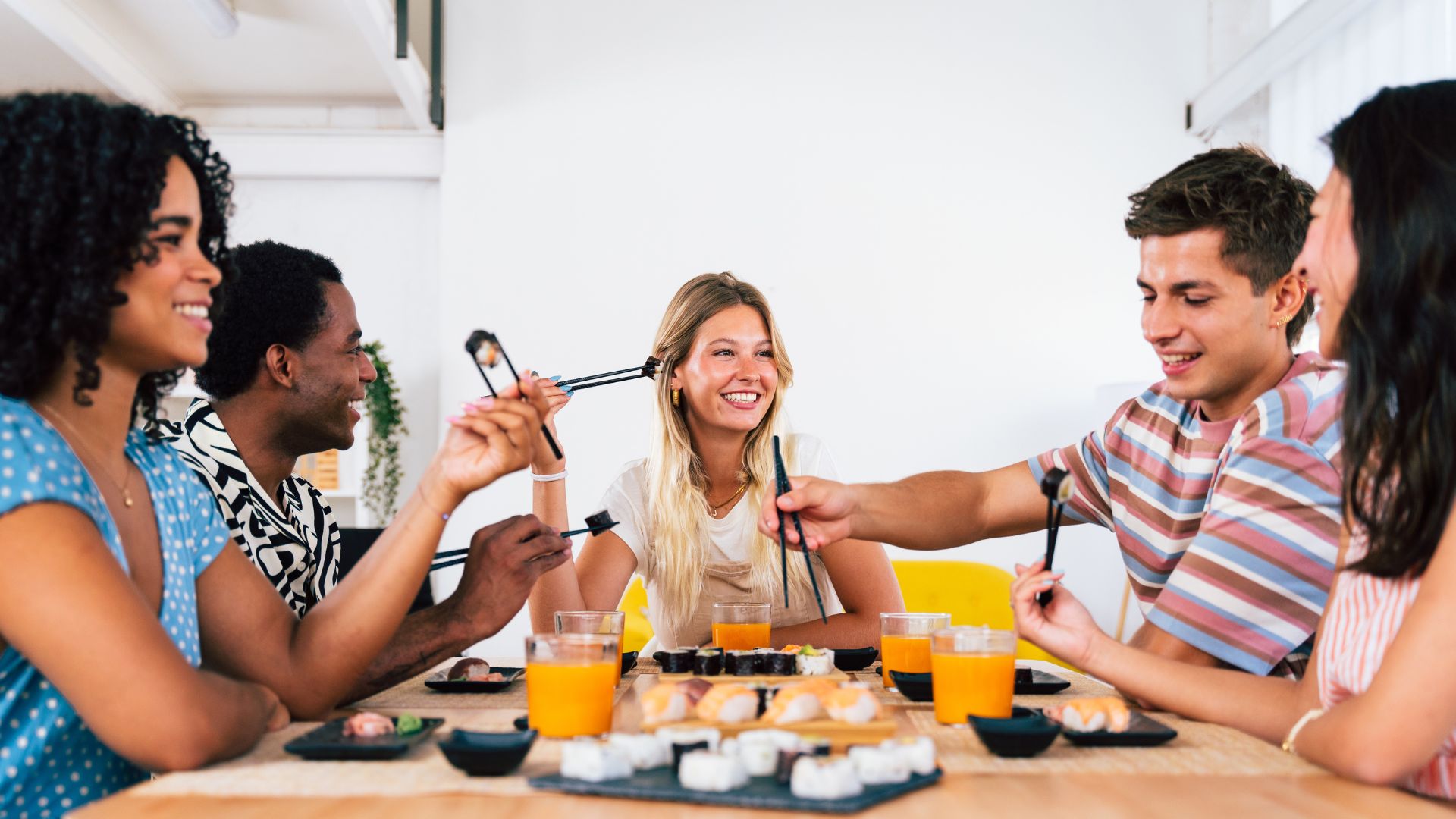 Group of people sharing sushi and drinks at a dining table, illustrating social interaction and potential infection risks for individuals with immunodeficiency.