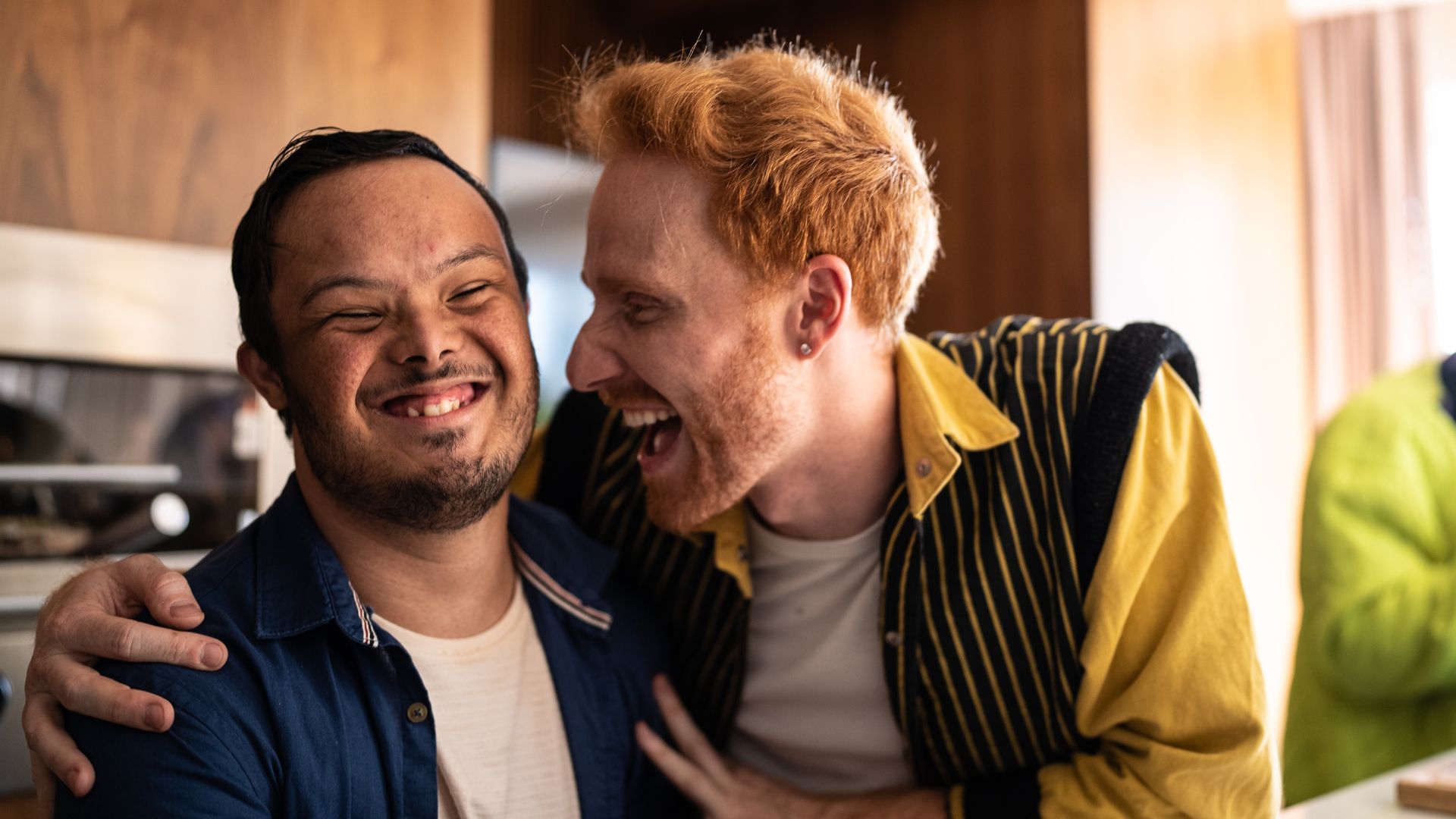 A man smiles with a friend in a workplace kitchen