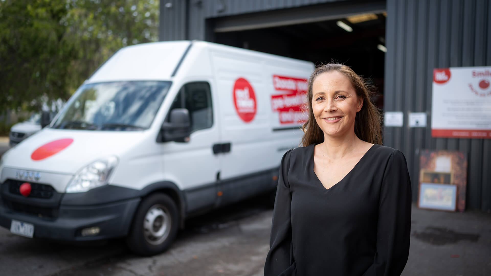 Woman smiling in black top outside business and in front of a white van