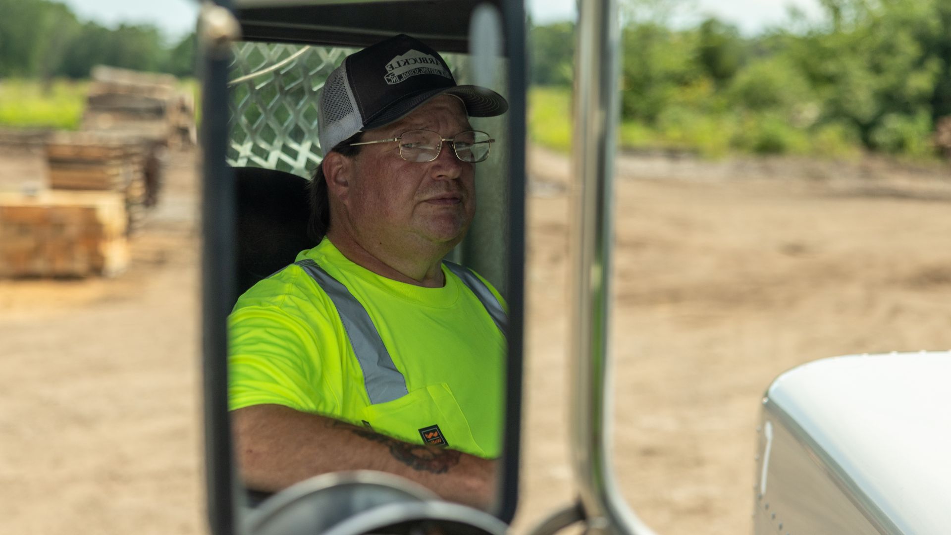 Ocie in a neon yellow shirt and a black cap with the 'Goodman' logo, sitting inside a vehicle and looking out thoughtfully.
