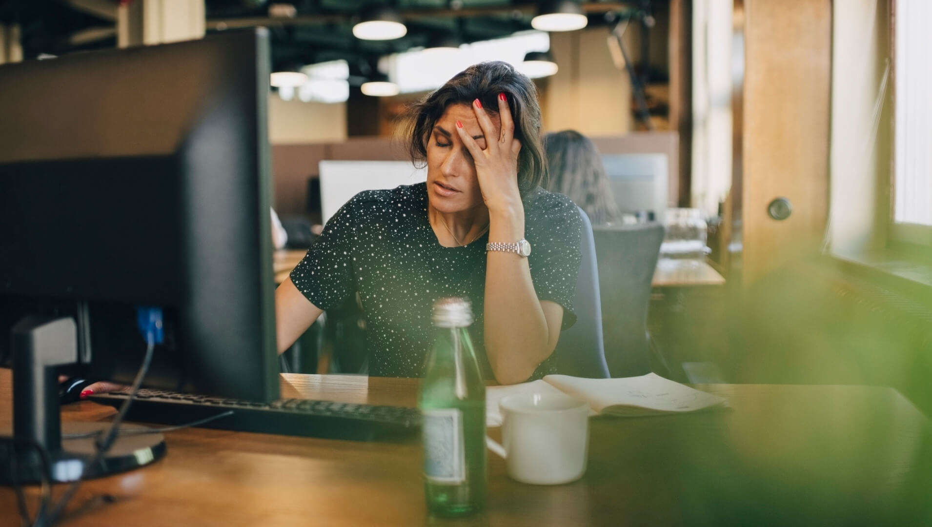 A woman has her hand on her head at a desk