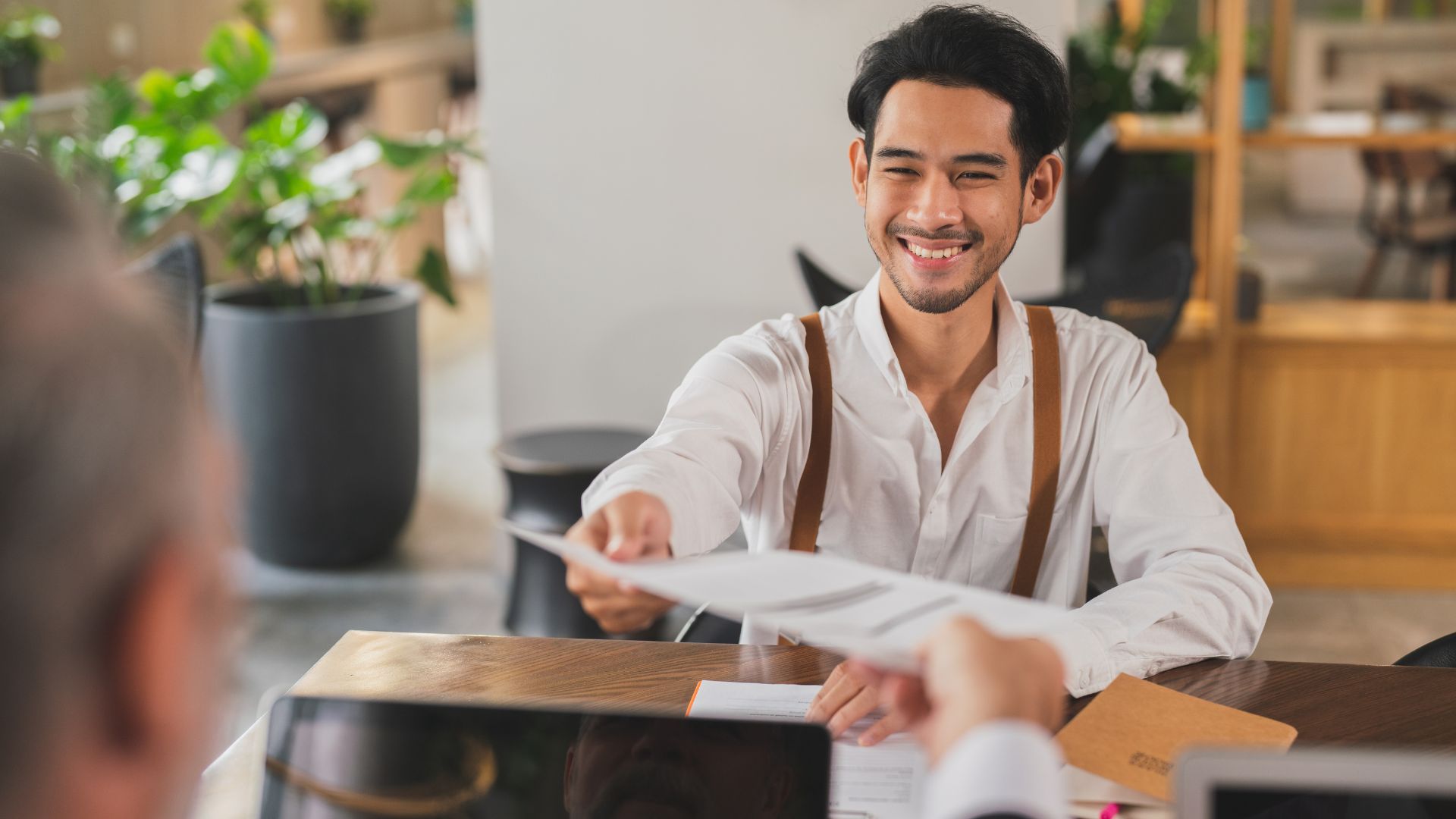 Job candidate handing a printed resume across a desk to an interviewer.
