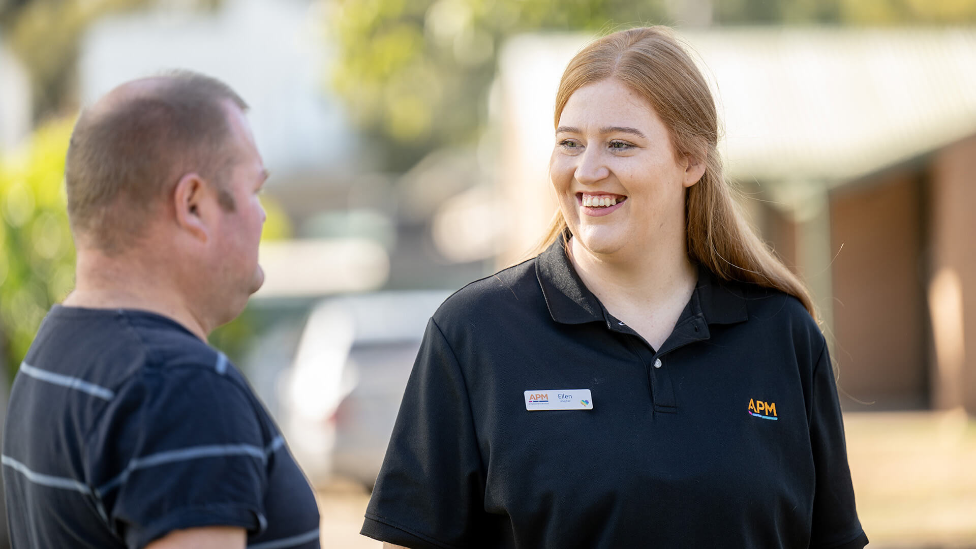 An APM employee in a black polo smiles in conversation with a DES participant