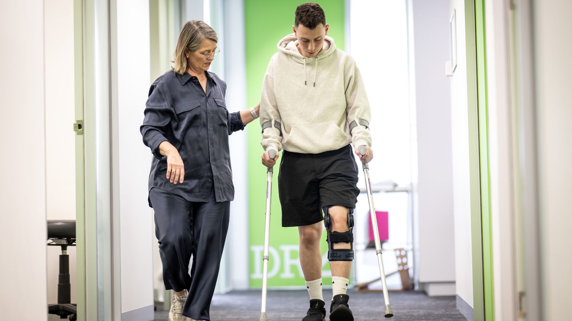 Dr Jane Rooney walks with a patient in crutches and a knee brace 