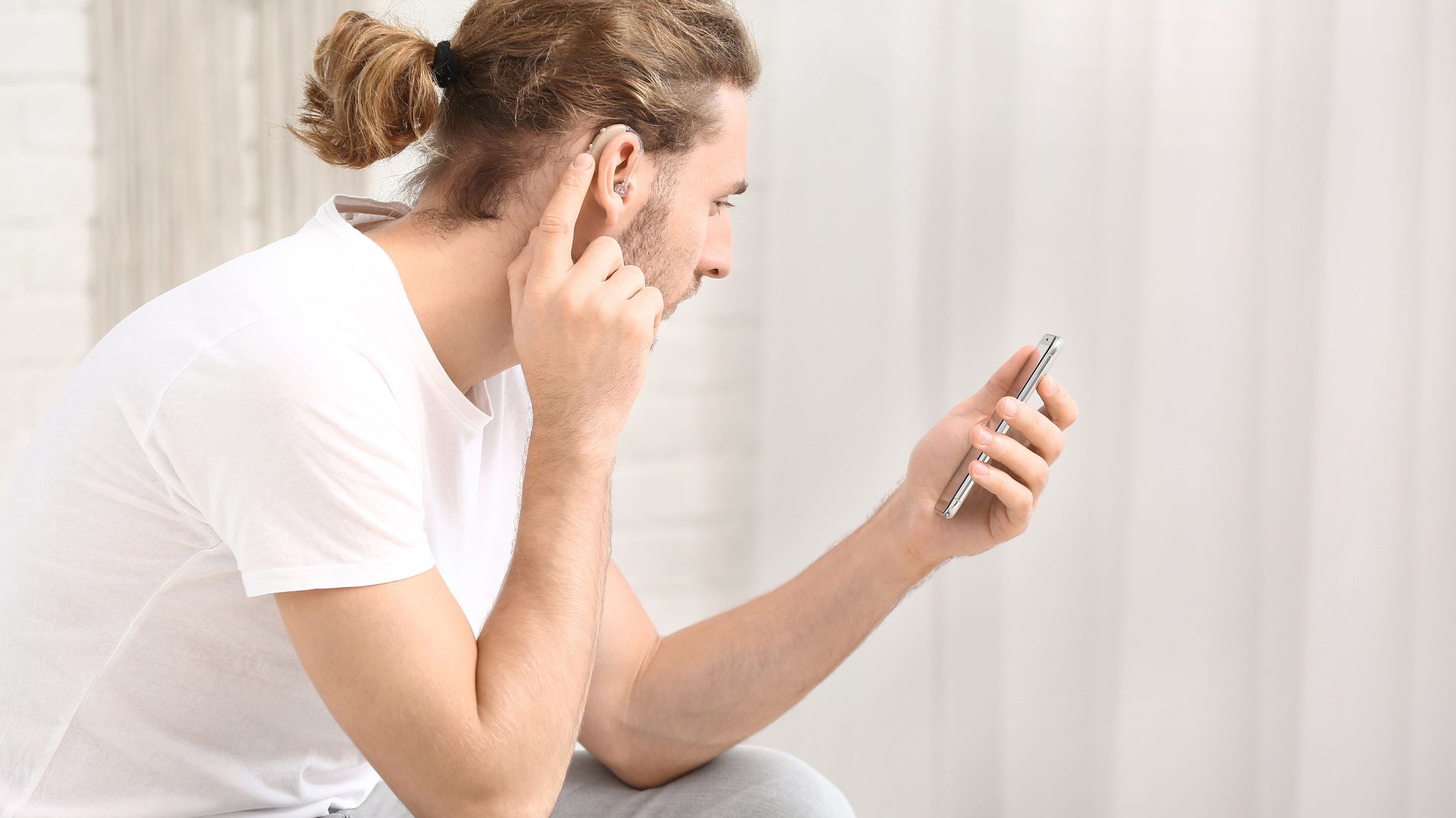 A man touches his hearing aid as he looks at his phone