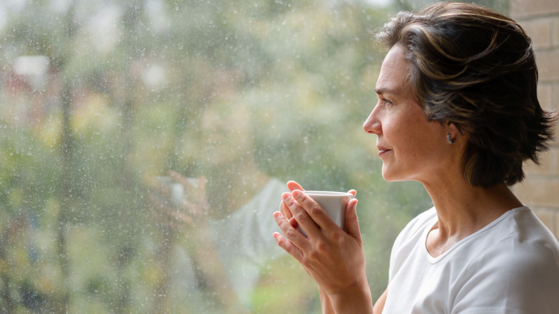 Person holding a cup and looking out a window, symbolising deep thinking and introspection common when questioning possible symptoms of schizophrenia.