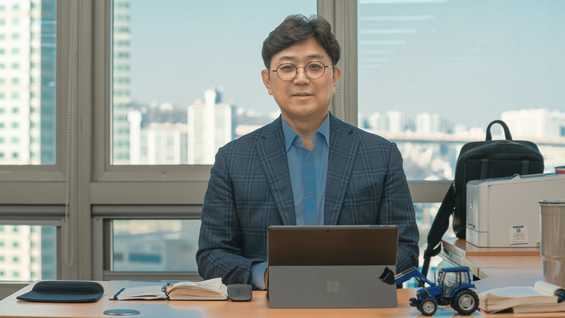 Sungjun Kim seated at a desk in a high-rise office environment, working on a laptop with notebooks and office supplies, symbolizing career planning and professional development.