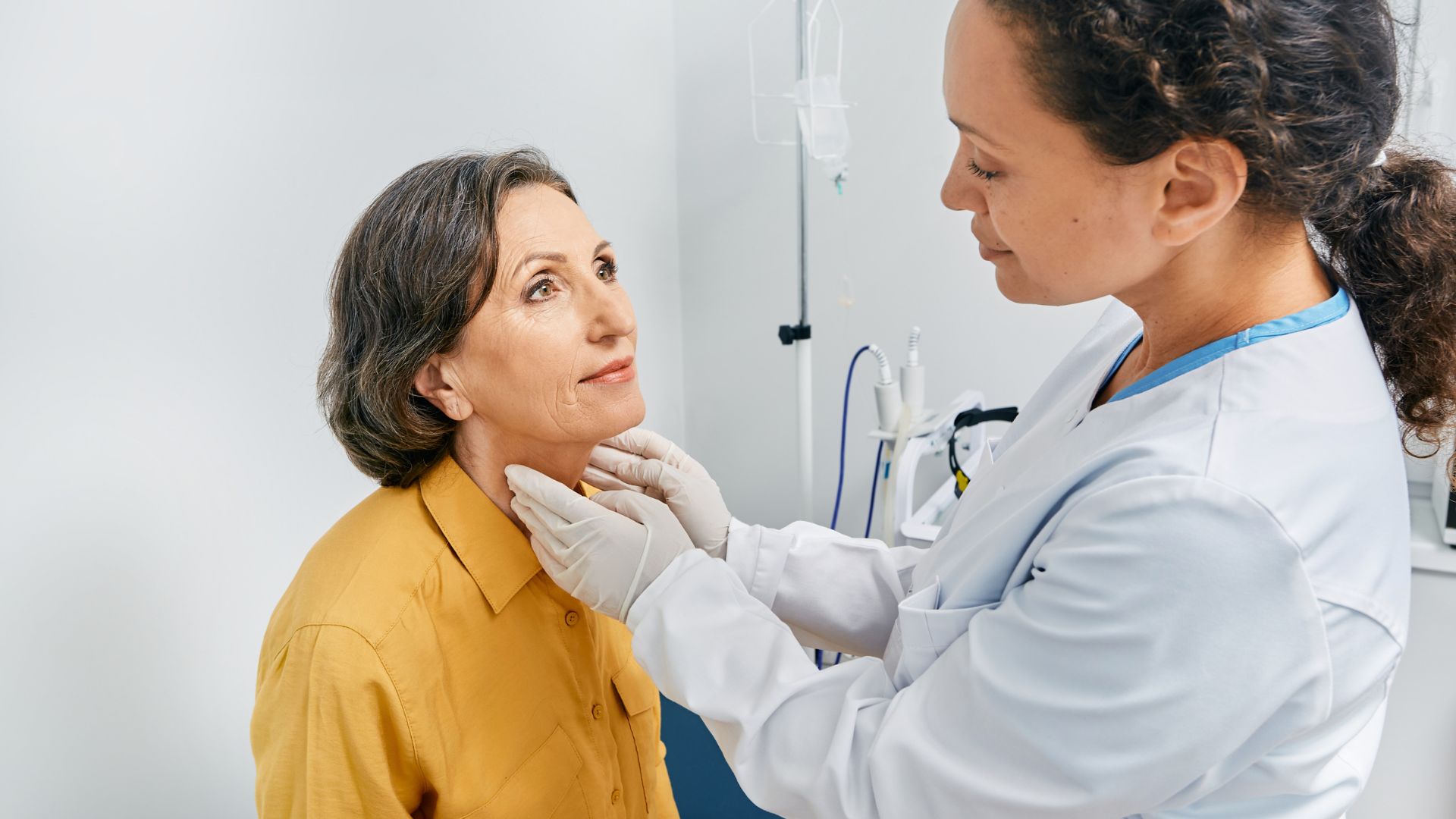 An older woman with a doctor feeling her thyroid