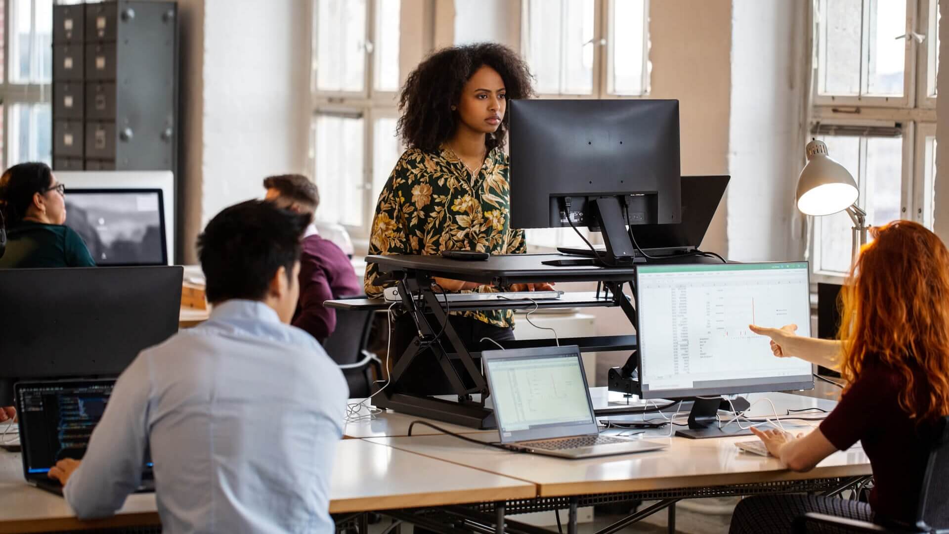 A woman using a standing desk in an open-plan office