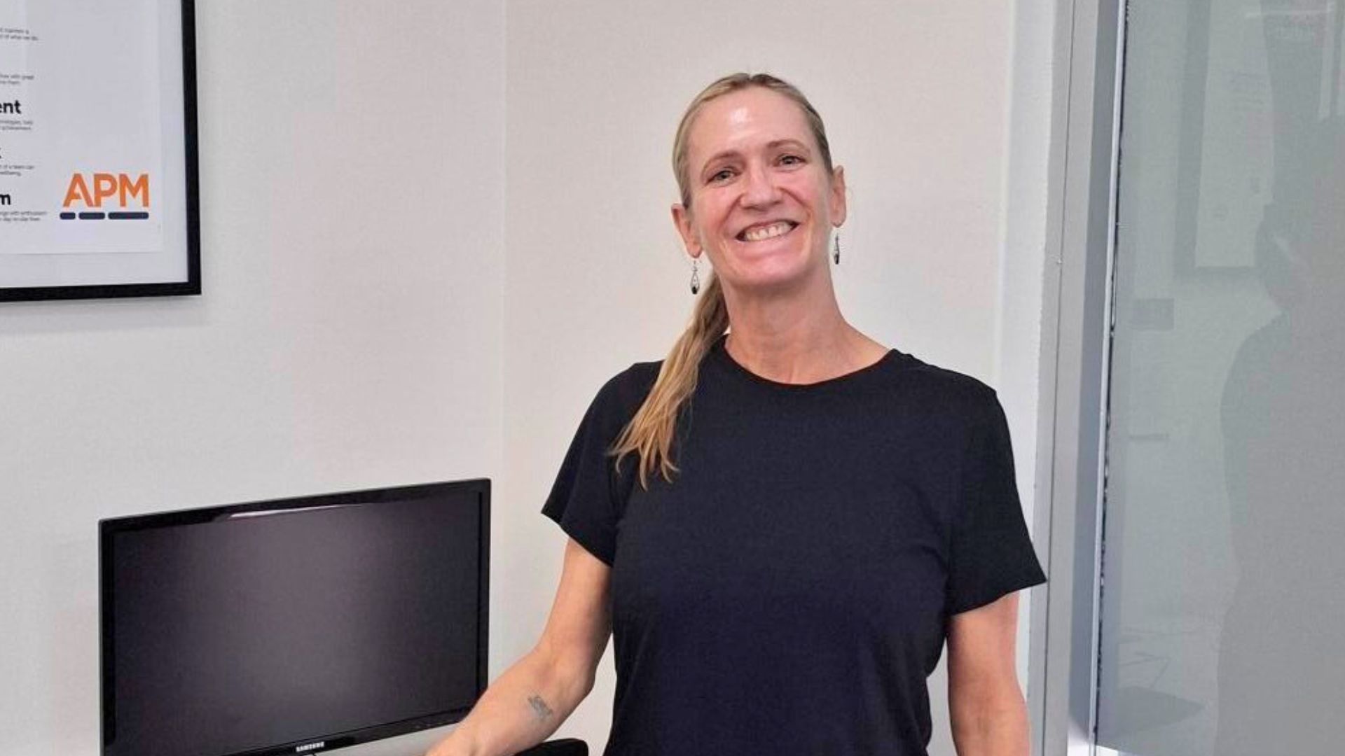 Katrina stands in a black dress smiling in an APM office