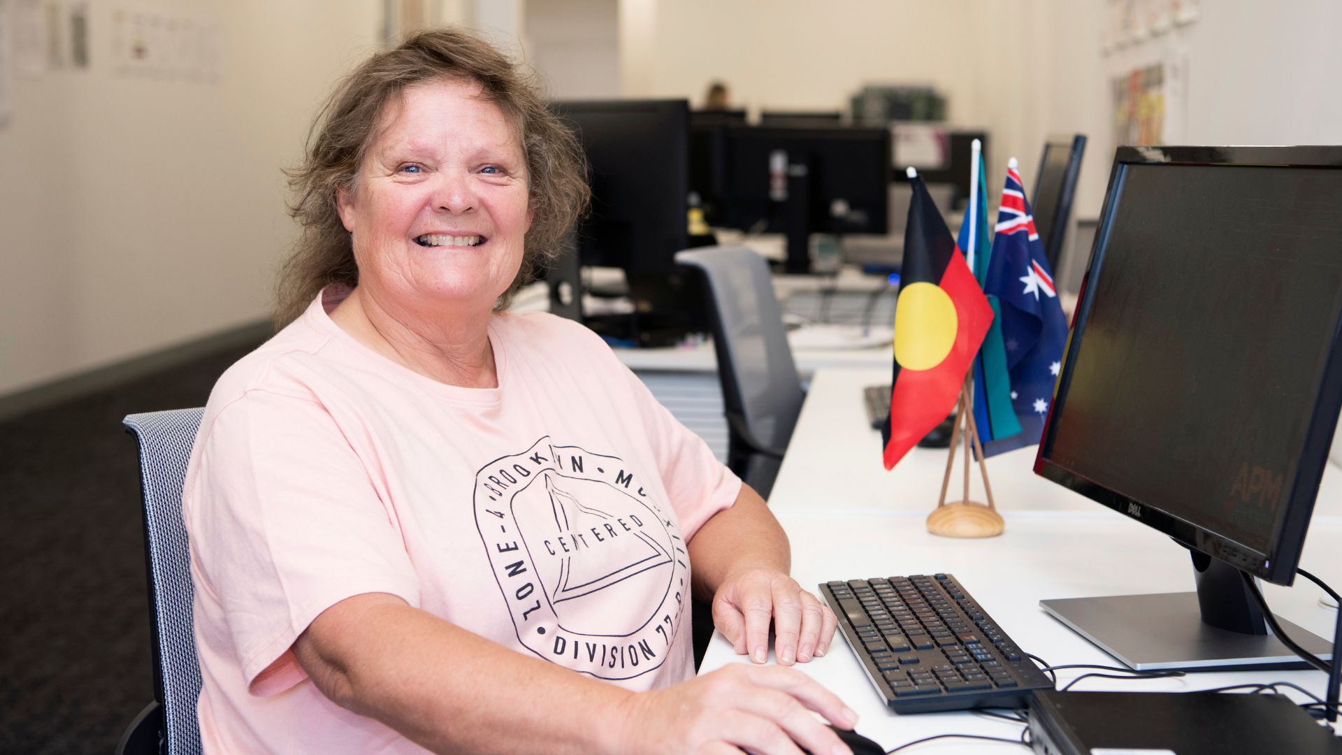 Smiling woman working at a desk using a computer in an office, with Australian and Aboriginal flags visible on the desk.