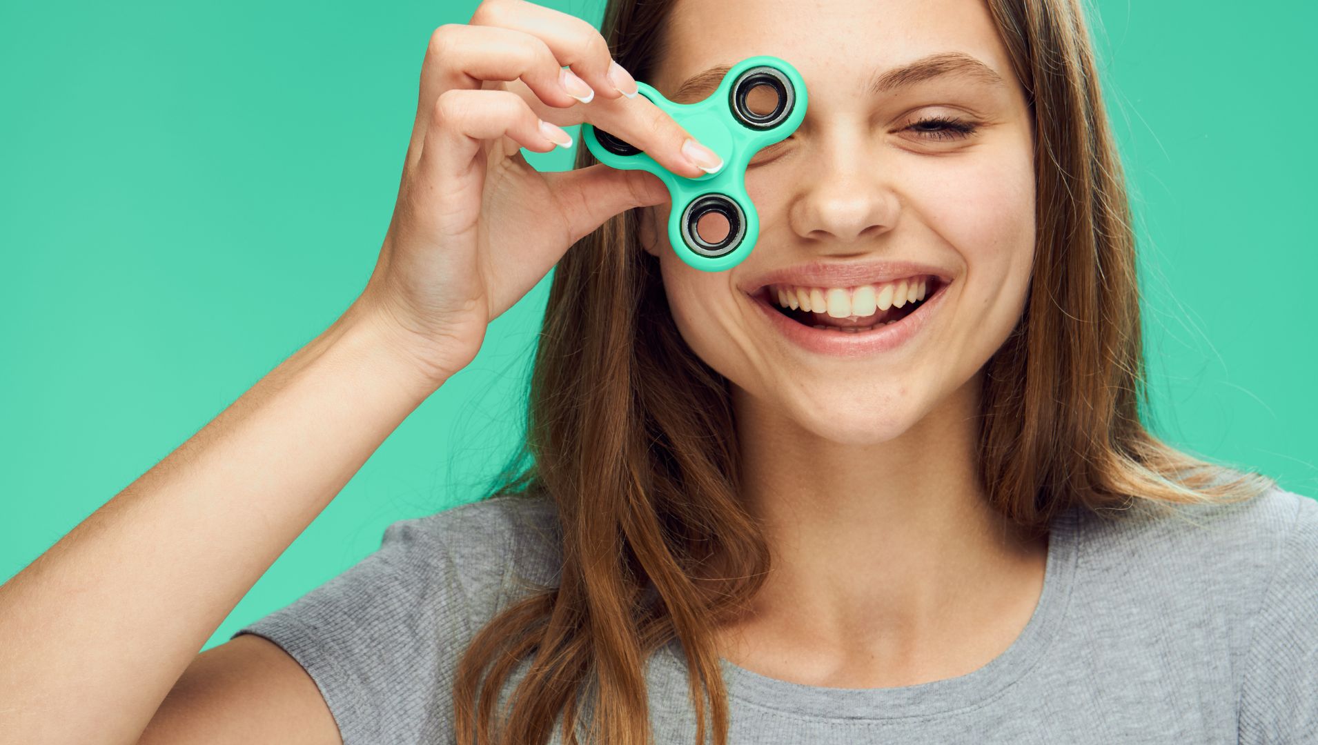 A smiling girl holds a fidget spinner over eye