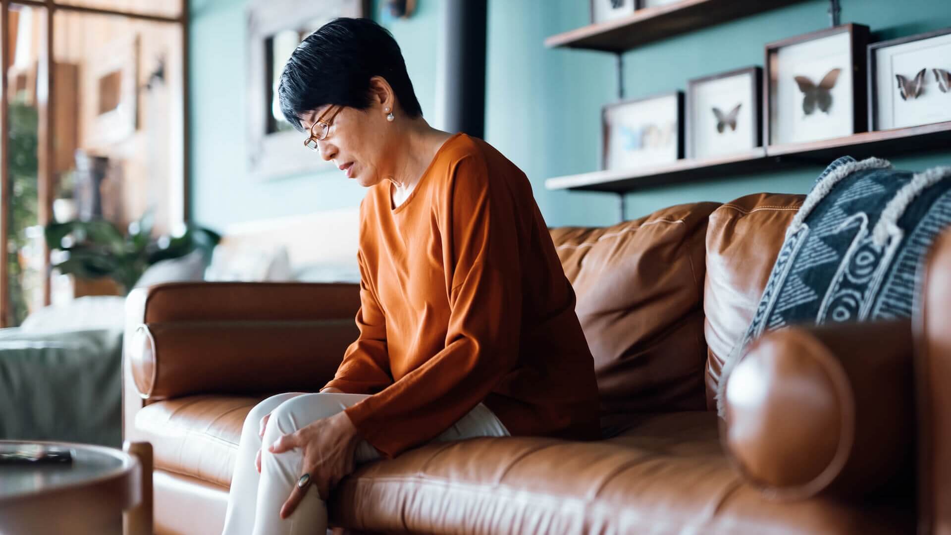 A woman grips her sore knee while sitting on the couch