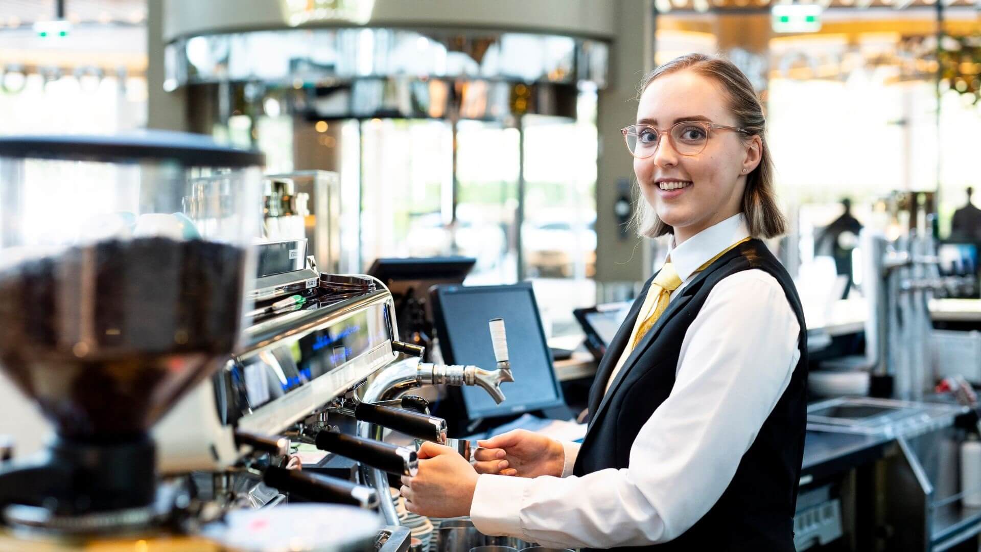 DES participant, Maegan, standing at a coffee machine and smiling while making coffee.