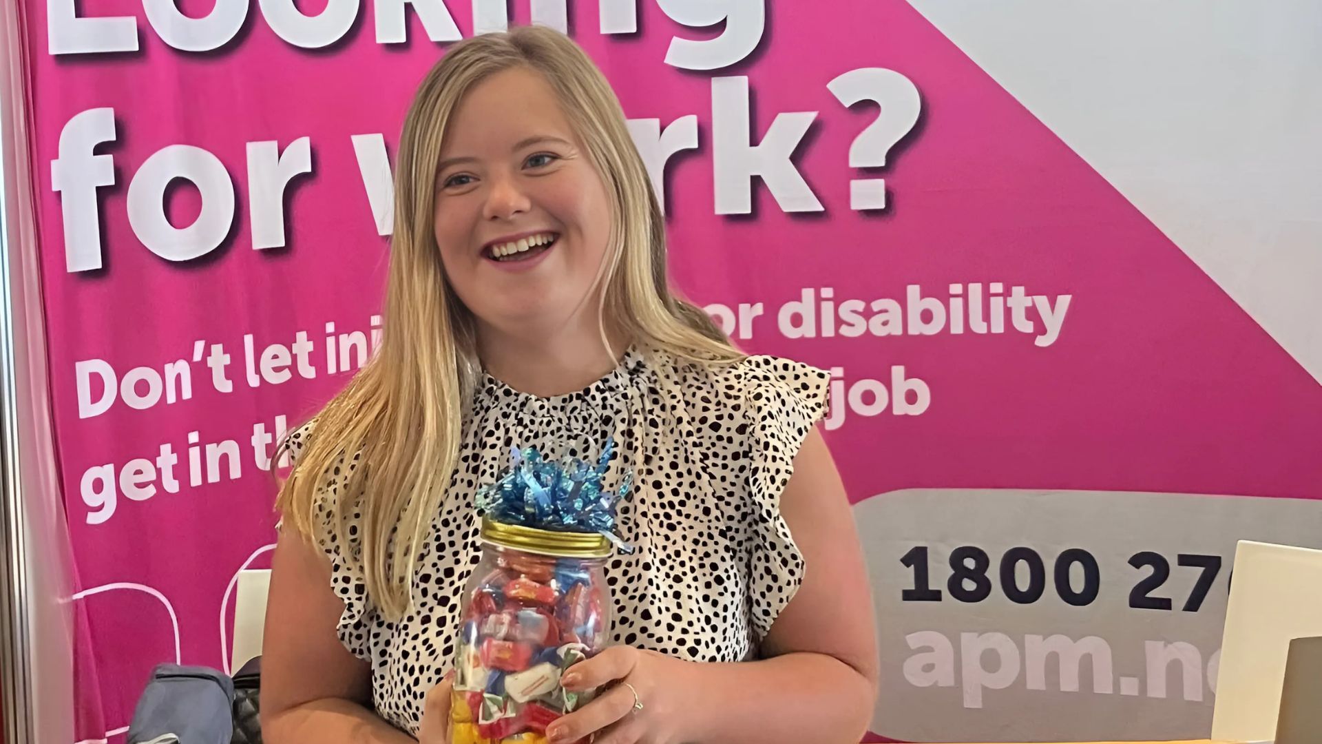 Woman with Down syndrome smiles next to APM booth