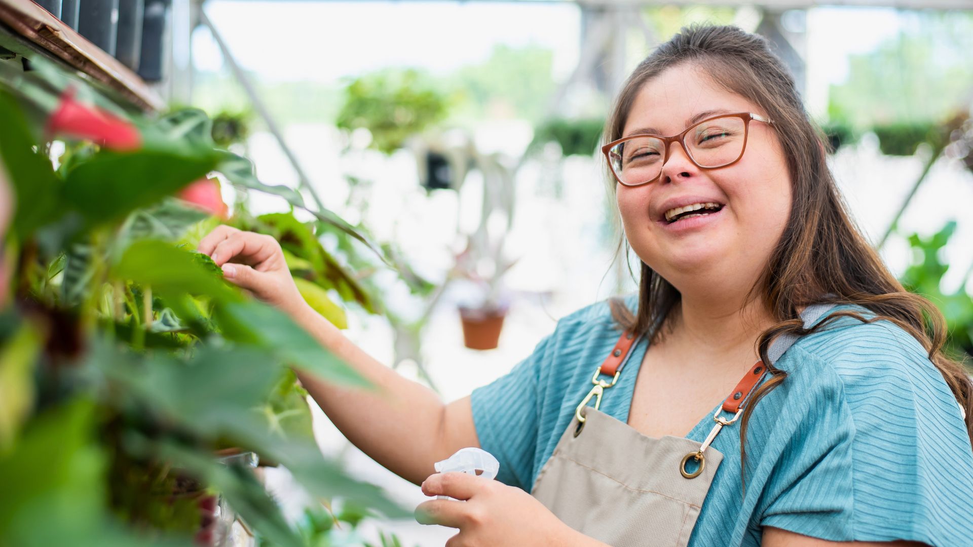 Person smiling while tending to plants in a greenhouse environment.