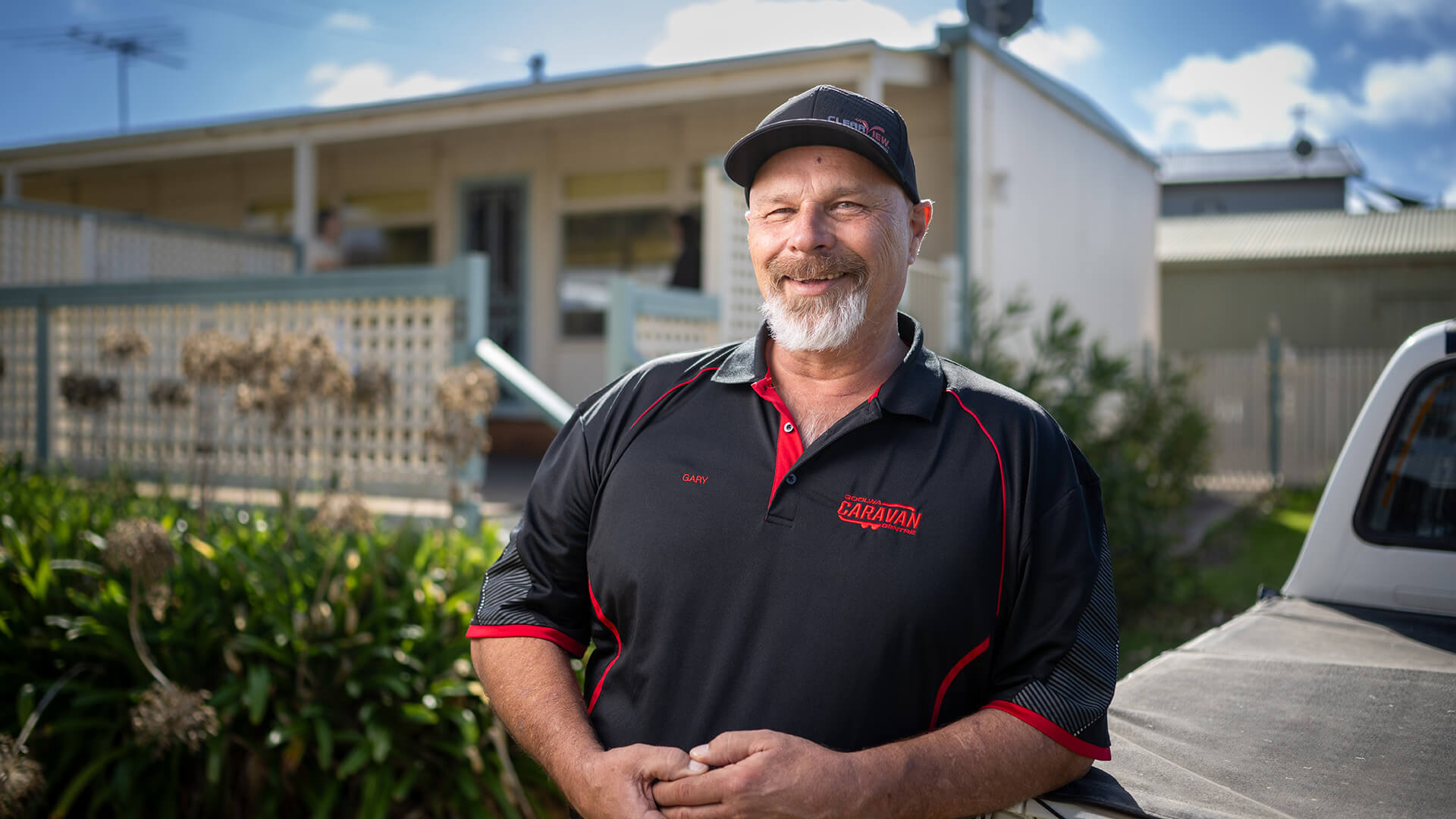 Gary a DES participant in a black shirt and cap smiles outside his home