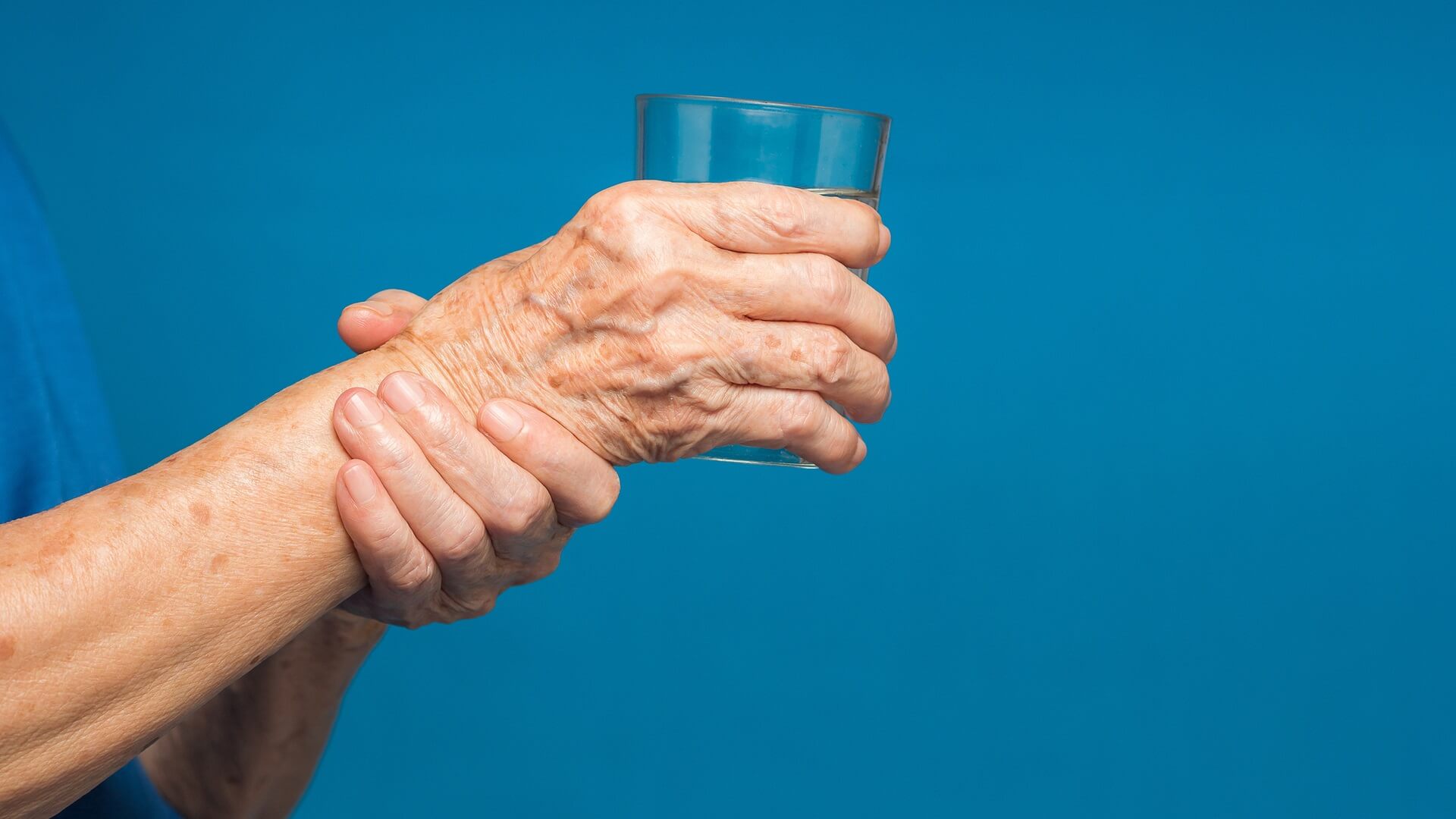 Close-up of hands senior woman trying to hold a glass of water