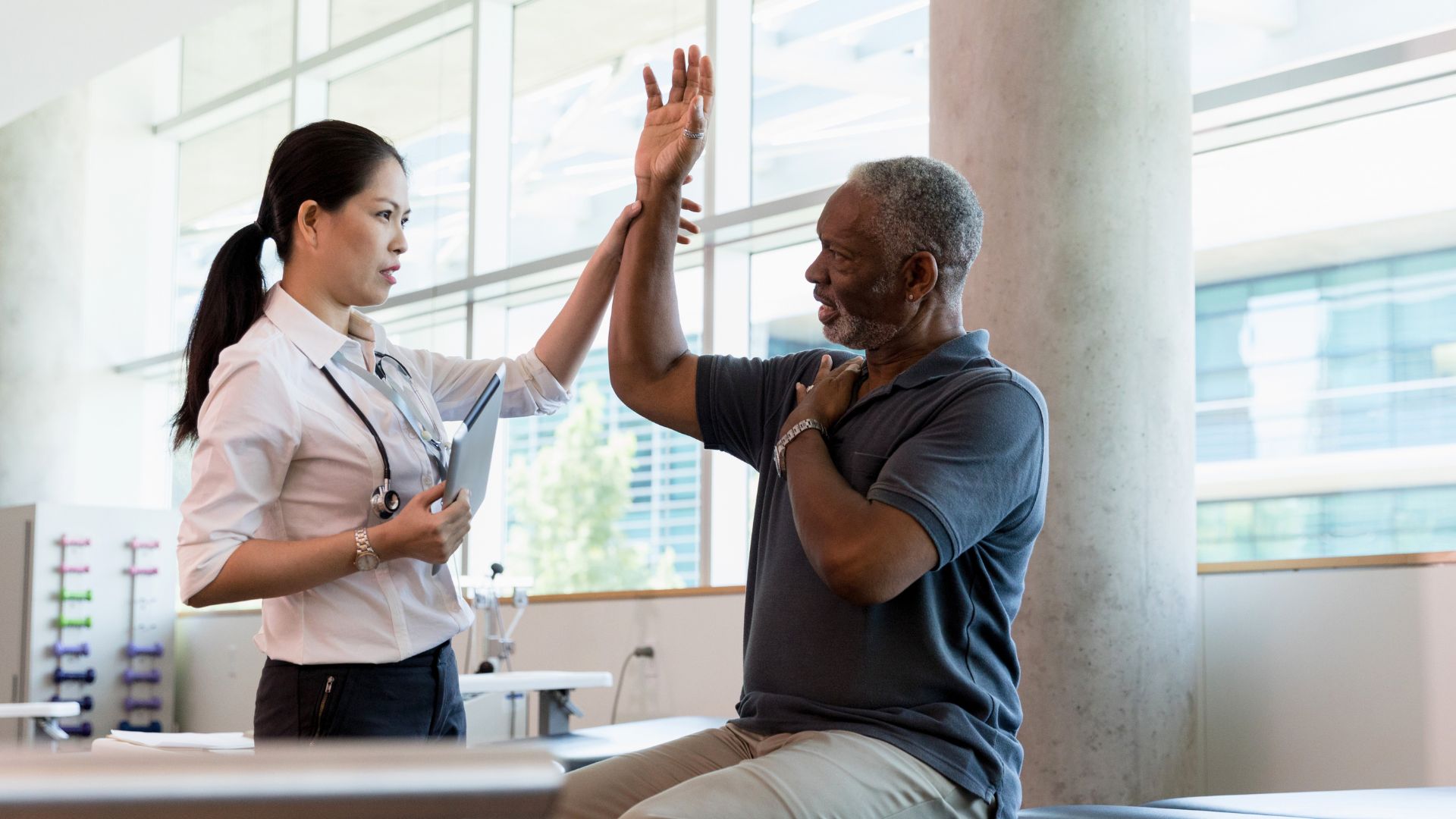  Physiotherapist assisting a man with shoulder movement exercises in a clinical setting.