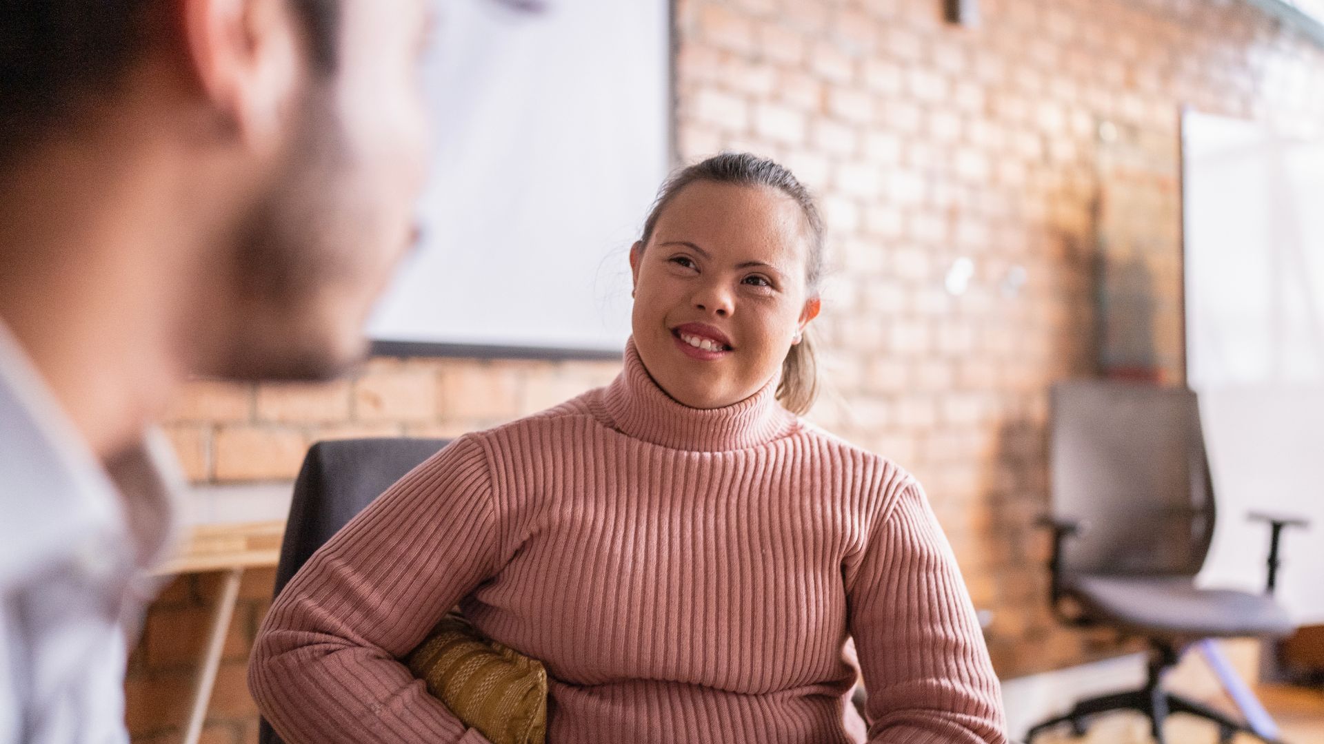 Person seated in an office, smiling during a conversation with another person