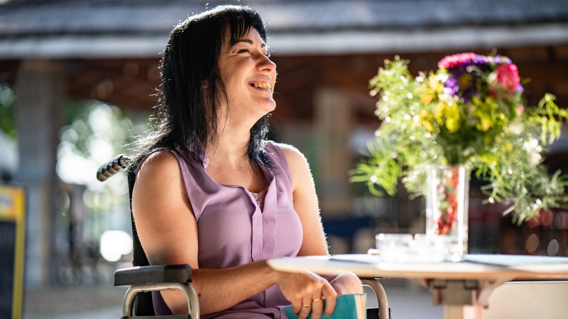 A person using a wheelchair seated at an outdoor table in a community setting, representing everyday life and the importance of accessing income support such as the Disability Support Pension in Australia.