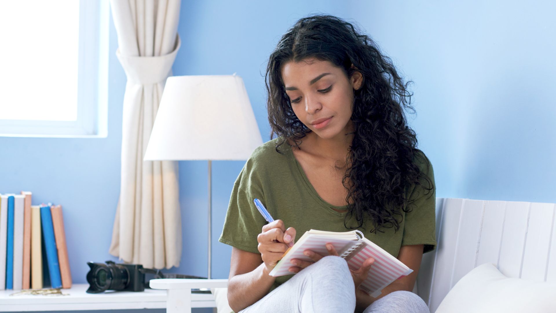 Person sitting on a couch writing in a notebook, representing health tracking and symptom monitoring for immunodeficiency.
