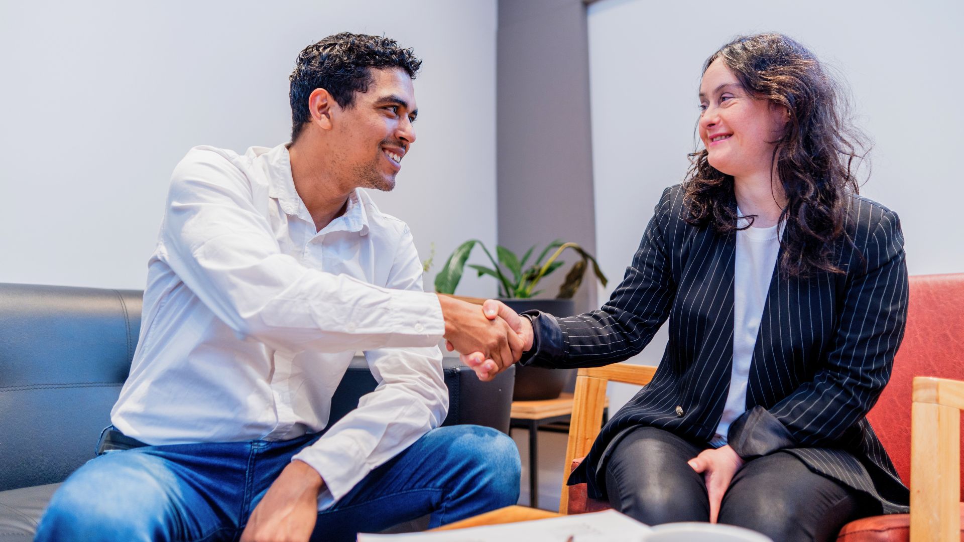 Two professionals smiling and shaking hands during a job interview meeting in a modern office setting.