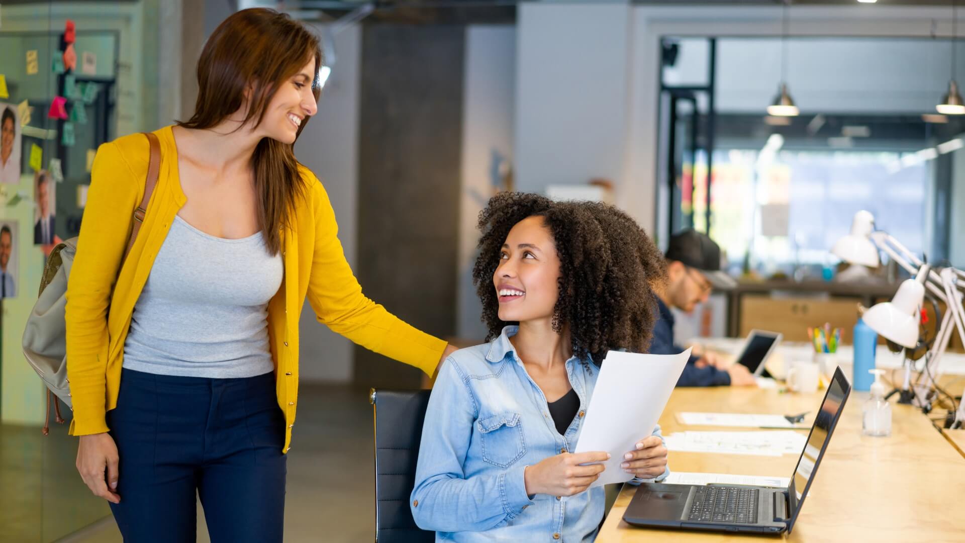 A woman talks to a co-worker as she walks past her desk