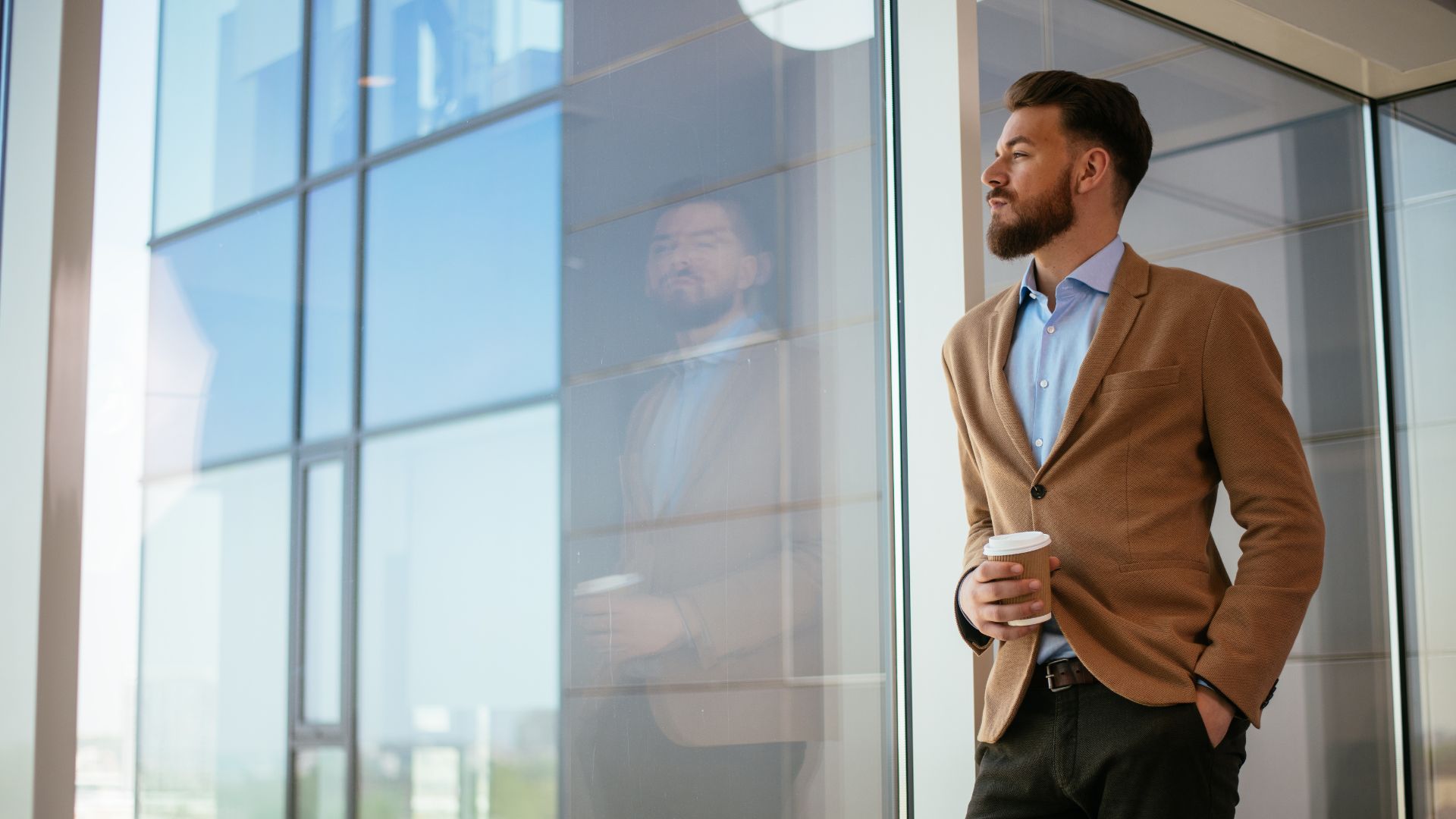 A male office worker takes a break and looks out a window while holding a coffee