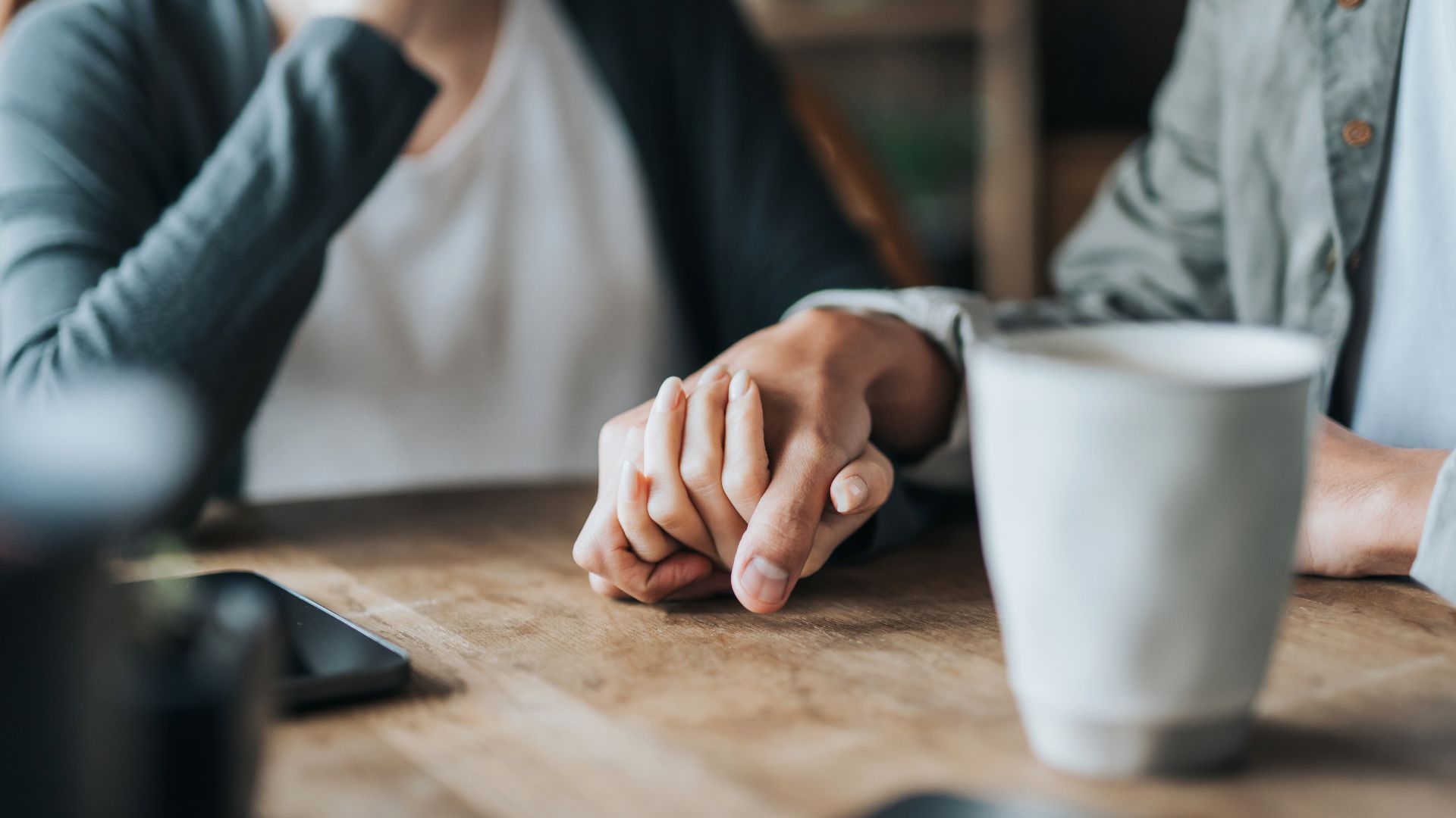 Two people holding hands at a table, emphasising emotional support and connection when seeking help for potential symptoms of schizophrenia.