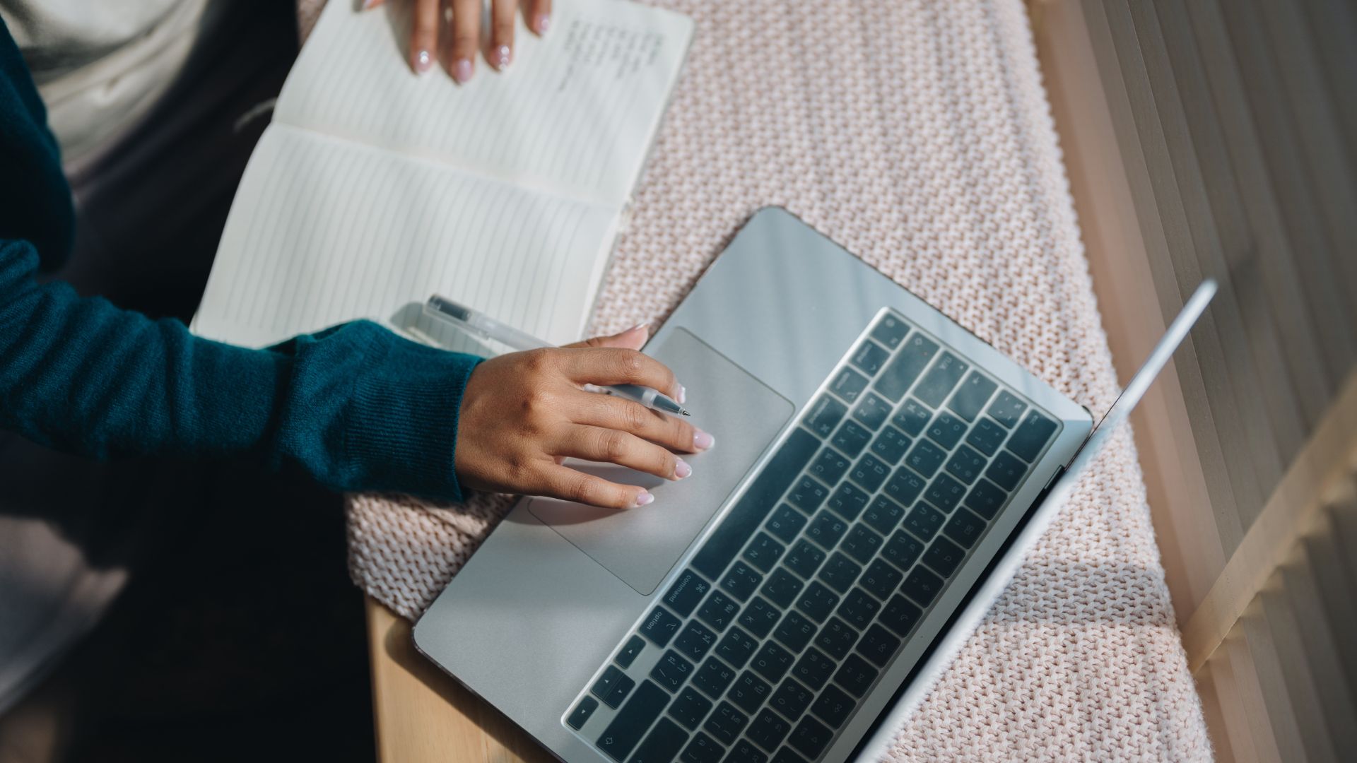 A person typing on a laptop keyboard next to an open notebook