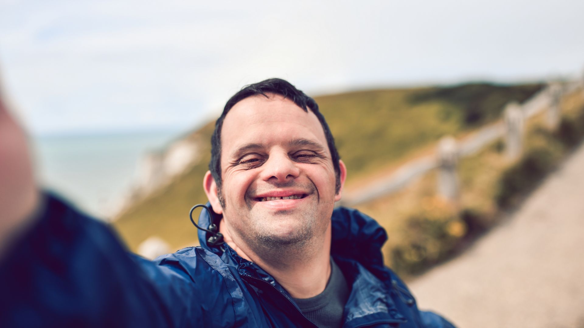 A man with disability smiles taking a selfie on a coastal footpath