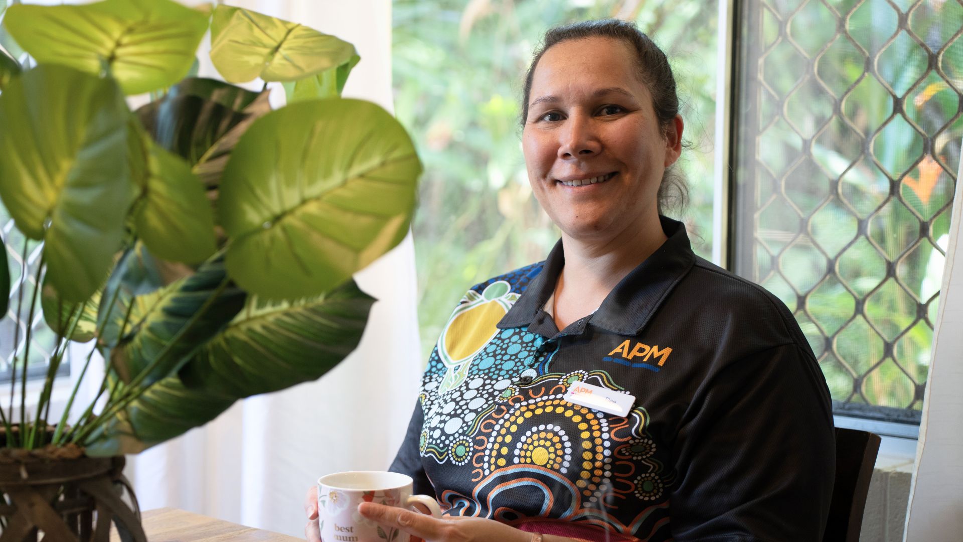 APM's Dee in a First Nations top sat at a table with a coffee