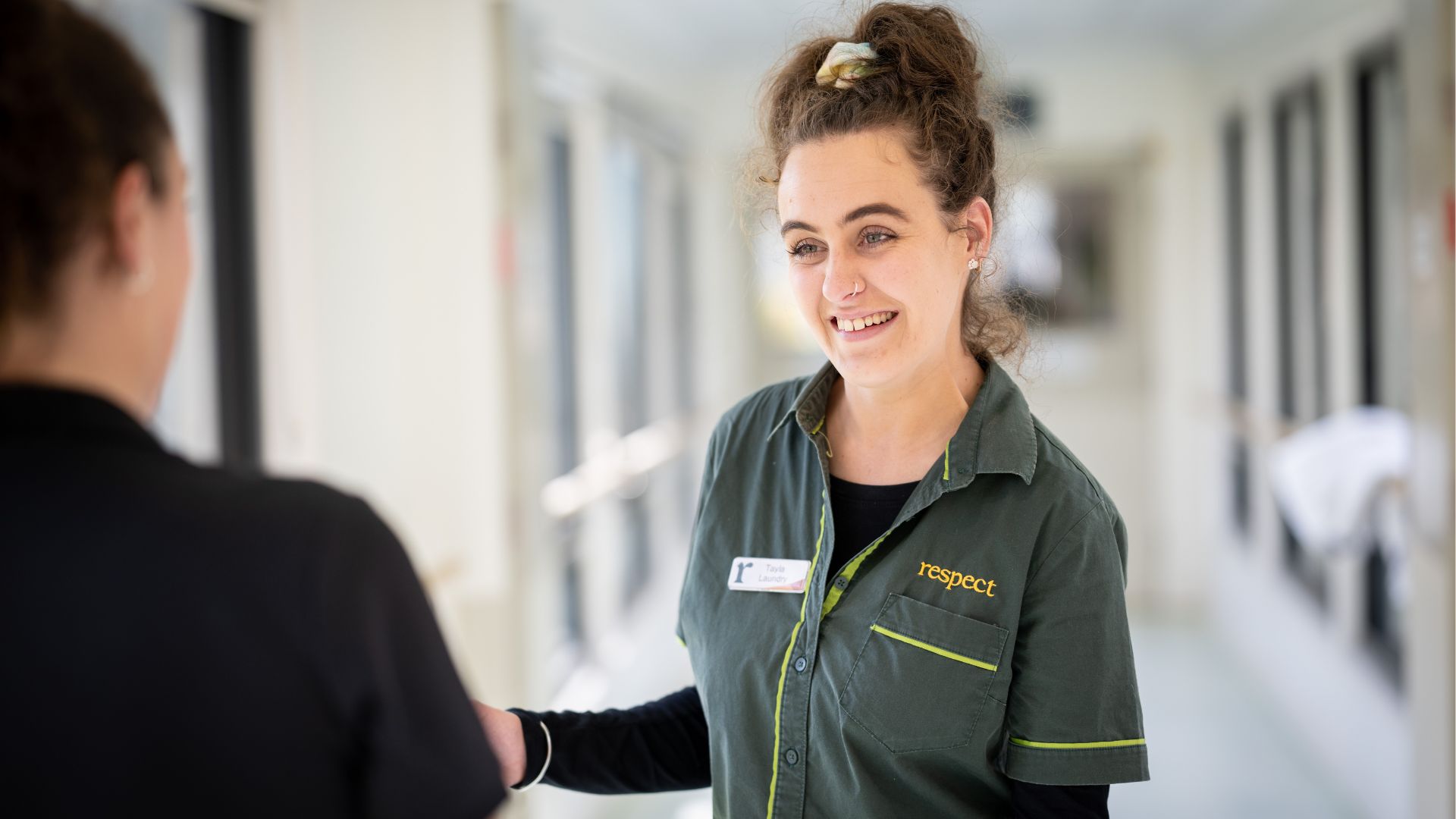  Employee in uniform speaking with another person in a corridor setting, showing the benefits of hiring people with disability in inclusive workplaces