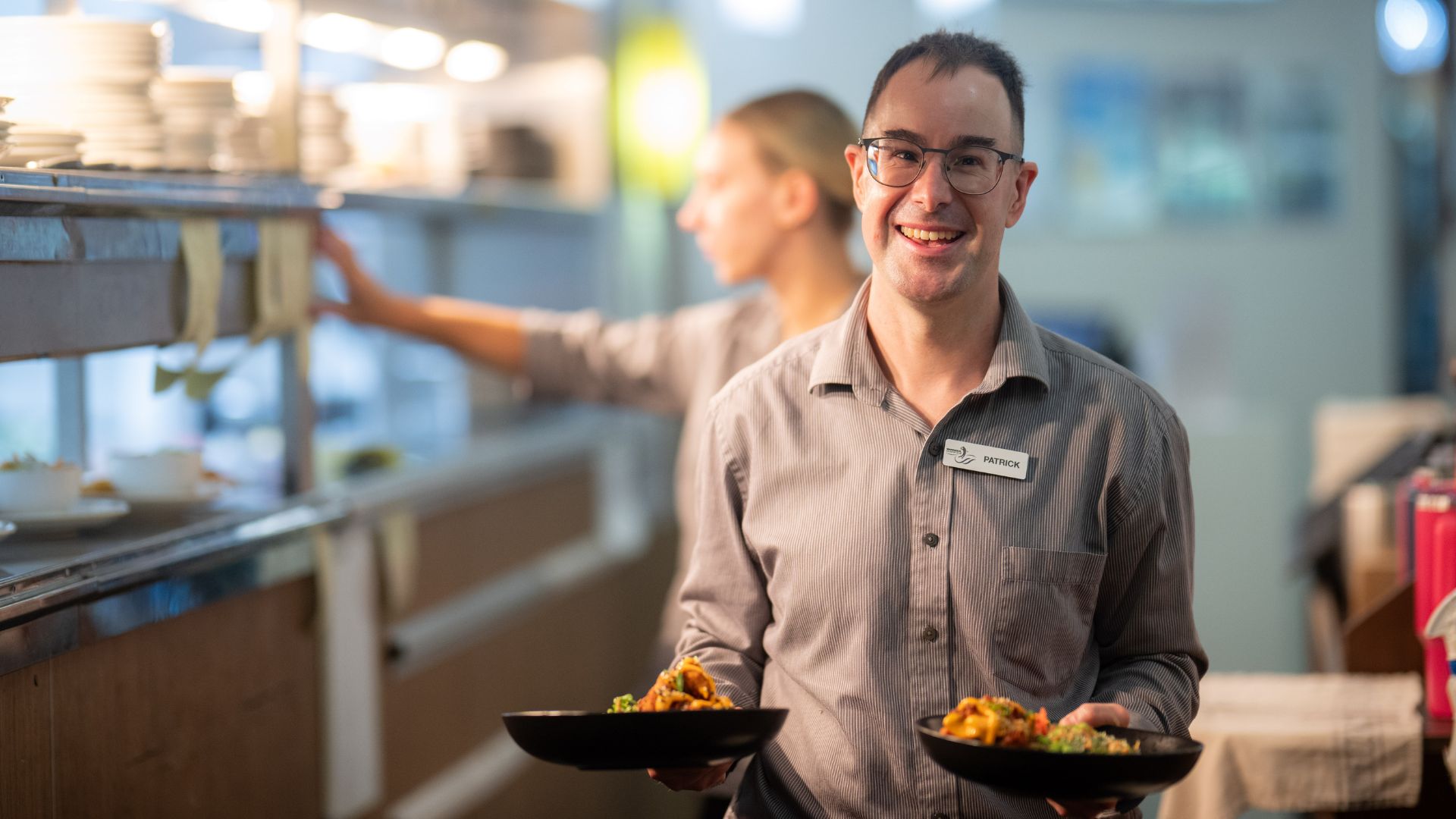 An employee holds a tray and smiles infront of a cafe counter