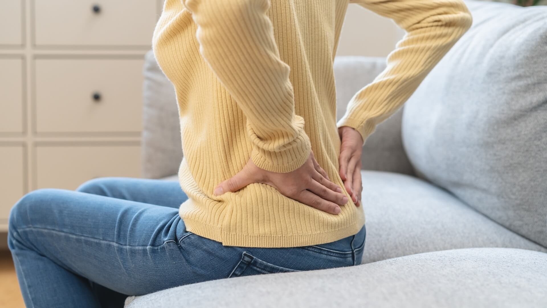A woman massaging her painful lower back as she sits on a coach