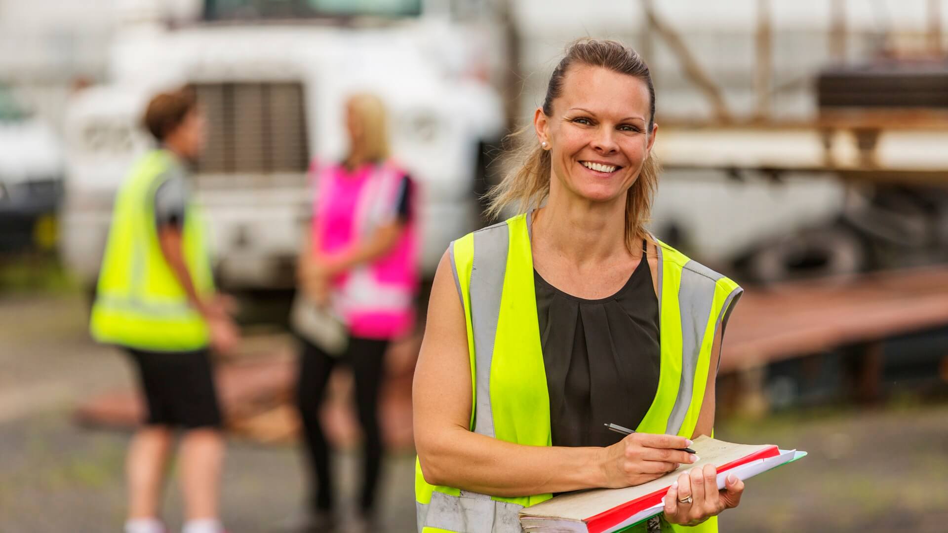 A woman in hi vis standing at a worksite smiling